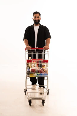 الاستفادة من الخصومات والتنزيلات على المنتجات، شراء المستلزمات والحاجيات الضرورية، الاستمتاع بالتسوق في المولات والمراكز التجارية، بورتريه لرجل عربي خليجي عماني يرتدي الزي الكاجوال يقف و عربة المشتريات أمامه ، الجسم بالطول الكامل، خلفية بيضاء
