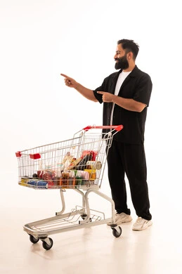 شراء المستلزمات والحاجيات الضرورية، الاستمتاع بالتسوق في المولات والمراكز التجارية، الاستفادة من الخصومات والتنزيلات على المنتجات، بورتريه لرجل عربي خليجي عماني يرتدي الزي الكاجوال يقف و عربة المشتريات أمامه ، الجسم بالطول الكامل، خلفية بيضاء