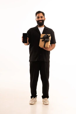 A display of a blank black screen, the concept of gratitude and appreciation, giving gifts during holidays and special occasions, expressing love, appreciation, and respect, a portrait of an Arab Gulf Omani man wearing casual attire holding a gift box while holding a mobile phone, looking with gestures of happiness, full-body, white background.