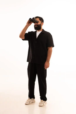 حب المغامرة والاستكشاف، رؤية الاشياء البعيدة عبر المنظار، بورتريه لشاب عربي خليجي عماني يرتدي الزي الكاجوال  ينظر من خلال المنظور ثنائي العينين يشير بإصبع السبابة الى شيء ما بإيماءات الفرح والسرور، خلفية بيضاء