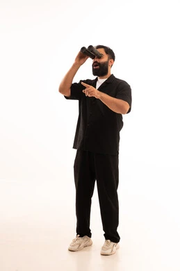 رؤية الاشياء البعيدة عبر المنظار، حب المغامرة والاستكشاف، بورتريه لشاب عربي خليجي عماني يرتدي الزي الكاجوال  ينظر من خلال المنظور ثنائي العينين يشير بإصبع السبابة الى شيء ما بإيماءات الفرح والسرور، خلفية بيضاء