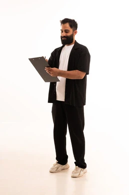 أدوات تدوين المهام اليومية،  تسجيل الملاحظات والمعلومات المهمة, بورتريه لرجل عربي خليجي عماني يرتدي الزي الكاجوال يمسك بيديه سنادة ورق سوداء وقلم يقوم بكتابة شيء بإيماءات التركيز والتمعن، الجسم بالطول الكامل، خلفية بيضاء