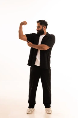 التمتع بالبنية الجسدية القوية، اللياقة البدنية والجسم الصحي المتين، بورتريه لرجل عربي خليجي عماني يرتدي الزي الكاجوال يقوم بعرض عضلات يديه ينظر الى الكاميرا بإيماءات القوة، صورة الجسم بالطول الكامل، خلفية بيضاء