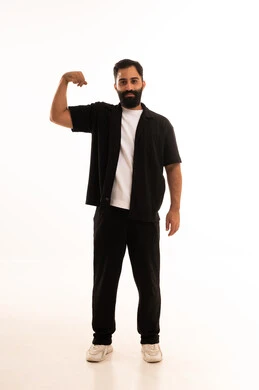 بورتريه لرجل عربي خليجي عماني يرتدي الزي الكاجوال يقوم بعرض عضلات يديه ينظر الى الكاميرا بإيماءات القوة، التمتع بالبنية الجسدية القوية، اللياقة البدنية والجسم الصحي المتين، صورة الجسم بالطول الكامل، خلفية بيضاء