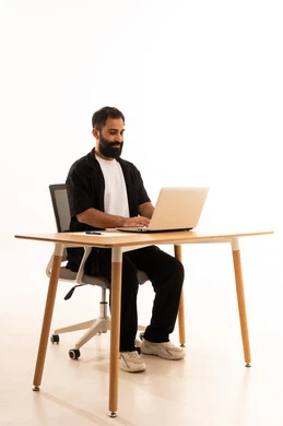 مشاهده الافلام والمسلسلات بتعابير السعاده ، دمج التقنيات الحديثة فى العمل، بورتريه لرجل عربي خليجي عماني يرتدي الزي الكاجوال يجلس على كرسي المكتب يعمل على جهاز الحاسوب المحمول ،اجراء بث مباشر عبر الجهاز اللوحى  ،  خلفية بيضاء