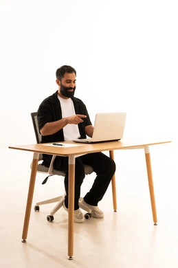 A portrait of an Arab Gulf Omani man wearing casual attire sitting on an office chair working on a laptop, integrating modern technologies in the administrative and office field, focusing on task completion, working in Omani offices and companies, with a white background.