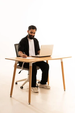 التركيز في إنجاز المهام، دمج التقنيات الحديثة بالمجال الإداري والمكتبي،العمل في المكاتب والشركات العمانية، بورتريه لرجل عربي خليجي عماني يرتدي الزى الكاجوال يجلس على كرسي المكتب يعمل على جهاز الحاسوب المحمول، خلفية بيضاء