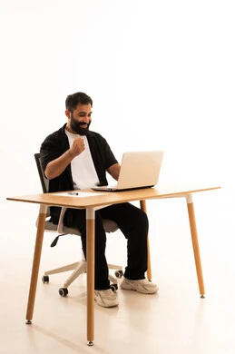 دمج التقنيات الحديثة بالمجال الإداري والمكتبي، التركيز في إنجاز المهام،العمل في المكاتب والشركات العمانية، بورتريه لرجل عربي خليجي عماني يرتدي الزى الكاجوال يجلس على كرسي المكتب يعمل على جهاز الحاسوب المحمول، خلفية بيضاء