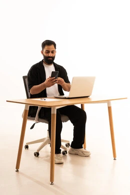 Browsing social media, making a phone call via mobile, focusing on completing tasks, integrating modern technologies in the administrative and office field, working in Omani offices and companies, a portrait of an Arab Gulf Omani man wearing casual attire sitting on an office chair and working on a laptop, white background.