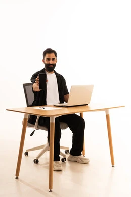 Browsing social media, making a phone call via mobile, focusing on completing tasks, integrating modern technologies in the administrative and office field, working in Omani offices and companies, a portrait of an Arab Gulf Omani man wearing casual attire sitting on an office chair and working on a laptop, white background.