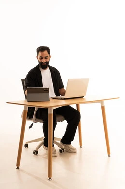 Conducting a live broadcast via the tablet, watching movies and series with expressions of happiness, integrating modern technologies in work, a portrait of an Arab Gulf Omani man wearing casual attire sitting on an office chair working on a laptop, white background.