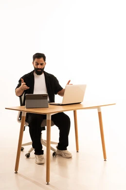Watching movies and series with expressions of happiness, integrating modern technologies in work, a portrait of an Arab Gulf Omani man wearing casual attire sitting on an office chair working on a laptop, conducting a live broadcast via a tablet, white background.