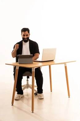 Conducting a live broadcast via the tablet, watching movies and series with expressions of happiness, integrating modern technologies in work, a portrait of an Arab Gulf Omani man wearing casual attire sitting on an office chair working on a laptop, white background.