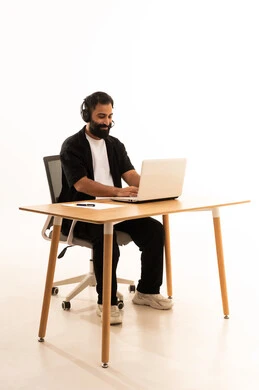 Focusing on task completion, integrating modern technologies in the administrative and office field, listening to music through headphones, working in Omani offices and companies, a portrait of an Arab Gulf Omani man wearing casual attire and headphones sitting on an office chair working on a laptop, white background.