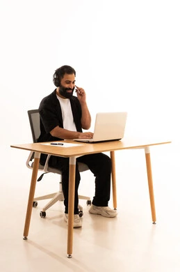 العمل في المكاتب والشركات العمانية،التركيز في إنجاز المهام، دمج التقنيات الحديثة بالمجال الإداري والمكتبي، سماع الموسيقي عبر سماعات الرأس،  بورتريه لرجل عربي خليجي عماني يرتدي الزى الكاجوال والهيدفون يجلس على كرسي المكتب يعمل على جهاز الحاسوب المحمول ، خلفية بيضاء