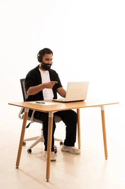Listening to music through headphones, focusing on completing tasks, integrating modern technologies in the administrative and office field, working in Omani offices and companies, a portrait of an Arab Gulf Omani man wearing casual attire and headphones sitting on an office chair working on a laptop, white background.