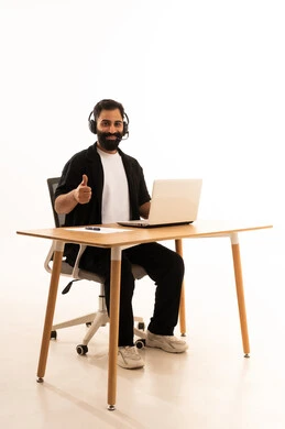 Focusing on task completion, integrating modern technologies in the administrative and office field, listening to music through headphones, working in Omani offices and companies, a portrait of an Arab Gulf Omani man wearing casual attire and headphones sitting on an office chair working on a laptop, white background.