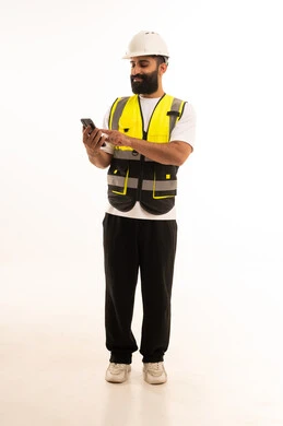 بورتريه لمهندس عربي خليجي عماني يرتدي الزى الكاجوال والخوذة وسترة الحماية يمسك الجوال بيده، تصفح مواقع التواصل الاجتماعي، استخدام التقنيات الحديثة بالقطاع الهندسي، دمج التكنولوجيا المتطورة بالعمل،الجسم بالطول الكامل، خلفية بيضاء