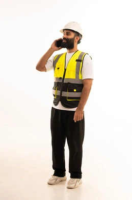 تصفح مواقع التواصل الاجتماعي، استخدام التقنيات الحديثة بالقطاع الهندسي، دمج التكنولوجيا المتطورة بالعمل، بورتريه لمهندس عربي خليجي عماني يرتدي الزى الكاجوال والخوذة وسترة الحماية يمسك الجوال بيده، الجسم بالطول الكامل، خلفية بيضاء