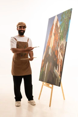 الاشارة الى اللوحة بتعابير السرور، استخدام ريشة التلوين، أنشطة ترفيهية فنية ممتعة، بورتريه لرسام عربي خليجي عماني يرتدي الزي الكاجوال وقبعة يحمل بيديه الالوان المائية, ورشة عمل وفنون, خلفية بيضاء