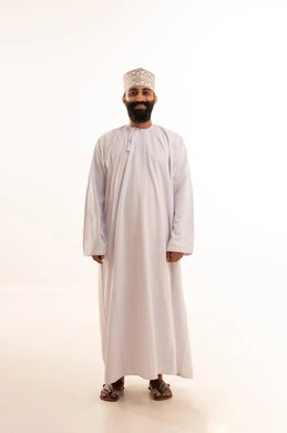 بورتريه لشاب عربي خليجي عماني يرتدي الدشداشة و الكمه ينظر بتعابير السعادة ،مفهوم الاناقة و الاهتمام بالمظهر الخارجي,  صورة الجسم بالطول الكامل, خلفية بيضاء
