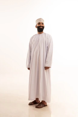 النظر الى شئ ما بايماءات السرور ، مفهوم الاناقة و الاهتمام بالمظهر الخارجي, بورتريه لشاب عربي خليجي عماني يرتدي الدشداشة و الكمه ينظر بتعابير السعادة ، صورة الجسم بالطول الكامل, خلفية بيضاء