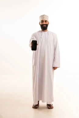 The use of modern and advanced technologies, gestures of happiness upon hearing good news, a portrait of an elderly Arab Gulf Omani man wearing a dishdasha and an Omani kumma, wearing reading glasses, holding a mobile phone in his hand and making a phone call, full-body shot, white background.