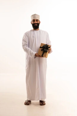 مفهوم الشكر والامتنان، تقديم الهدايا بالاعياد والمناسبات الخاصة، التعبير عن الحب والتقدير والاحترام، بورتريه لرجل عربي خليجي عماني يرتدي الدشداشة والكمة يحمل صندوق هدية ينظر بايماءات السعادة، الجسم بالطول الكامل، خلفية بيضاء