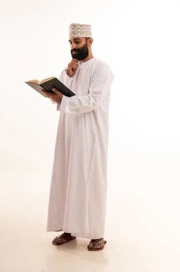 ثقافة التعلم الذاتي ، قراءة الكتب بتمعن، بورترية لشاب عربي خليجي عماني يرتدي الدشداشة و الكمة يمسك بيده كتاب تثقيفي ، الاستمتاع بقراءة الروايات والقصص، خلفية بيضاء