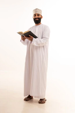 قراءة الكتب بتمعن، ثقافة التعلم الذاتي ، بورترية لشاب عربي خليجي عماني يرتدي الدشداشة و الكمة يمسك بيده كتاب تثقيفي ، الاستمتاع بقراءة الروايات والقصص، خلفية بيضاء