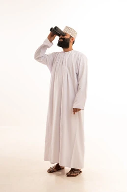 A portrait of a young Arab Gulf Omani man wearing a dishdasha and kumma, looking through a binocular, pointing with his index finger at something with gestures of joy and happiness, seeing distant things through the binoculars, a love for adventure and exploration, white background.