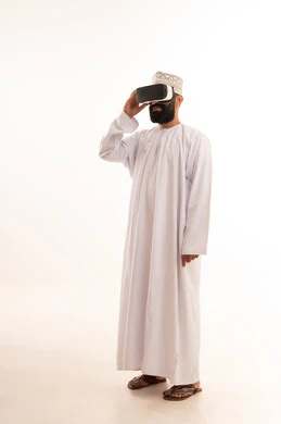 ارتداء نظارات الواقع الافتراضي,تعابير الاندماج والتفاعل، محاكاة العالم الخيالي, استخدام الأجهزة التقنية الحديثة, بورتريه لرجل عربي خليجي عماني يرتدي الدشداشة والكمة يضع نظارة الفي ار ثلاثية الأبعاد، قضاء وقت ممتع باللعب في العاب الفيديو ، خلفية بيضاء