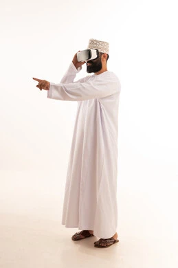 محاكاة العالم الخيالي, تعابير الاندماج والتفاعل،ارتداء نظارات الواقع الافتراضي, استخدام الأجهزة التقنية الحديثة, بورتريه لرجل عربي خليجي عماني يرتدي الدشداشة والكمة يضع نظارة الفي ار ثلاثية الأبعاد، قضاء وقت ممتع باللعب في العاب الفيديو ، خلفية بيضاء