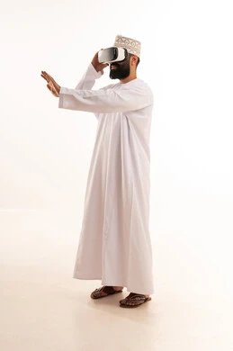 تعابير الاندماج والتفاعل، محاكاة العالم الخيالي, ارتداء نظارات الواقع الافتراضي, استخدام الأجهزة التقنية الحديثة, بورتريه لرجل عربي خليجي عماني يرتدي الدشداشة والكمة يضع نظارة الفي ار ثلاثية الأبعاد، قضاء وقت ممتع باللعب في العاب الفيديو ، خلفية بيضاء