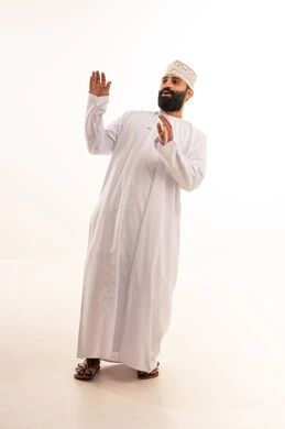 Request to stop, refrain, and not approach, protecting oneself from external harm, a portrait of an Arab Gulf Omani man wearing a dishdasha and kumma looking at something above and raising his hands with expressions of fear and retreat, full-body, white background.