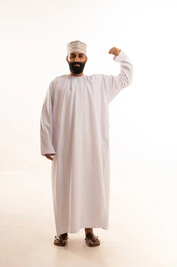 اللياقة البدنية والجسم الصحي المتين،التمتع بالبنية الجسدية القوية،  بورتريه مقرب لرجل عربي خليجي عماني يرتدي الدشداشة والكمه يقوم بعرض عضلات يديه ينظر الى الكاميرا بإيماءات القوة، صورة الجسم بالطول الكامل، خلفية بيضاء