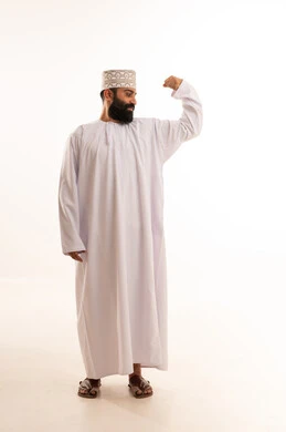 التمتع بالبنية الجسدية القوية، اللياقة البدنية والجسم الصحي المتين، بورتريه مقرب لرجل عربي خليجي عماني يرتدي الدشداشة والكمه يقوم بعرض عضلات يديه ينظر الى الكاميرا بإيماءات القوة، صورة الجسم بالطول الكامل، خلفية بيضاء