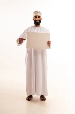 إعلانات وعروض تسويقية، ايماءات السعادة والسرور،استخدام لوحات توضيحية ووسائل تعليمية، بورتريه لرجل عربي خليجي عماني مبتسم يرتدي الدشداشه والكمة يحمل بيده لوح ابيض (موك اب فارغ)، الطول الكامل للجسم، خلفية بيضاء.