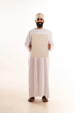 النظر الى الكاميرا بتعابير السعادة والسرور، إعلانات وعروض تسويقية، استخدام لوحات توضيحية ووسائل تعليمية، بورتريه لرجل عربي خليجي عماني مبتسم يرتدي الدشداشه والكمة يحمل بيده لوح ابيض (موك اب فارغ)، الطول الكامل للجسم، خلفية بيضاء.