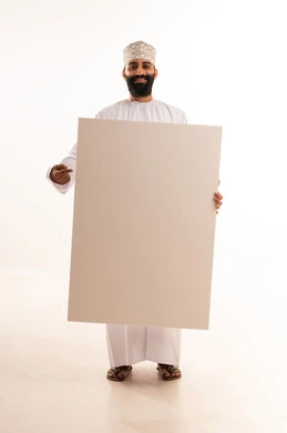 إعلانات وعروض تسويقية، ايماءات السعادة والسرور،استخدام لوحات توضيحية ووسائل تعليمية، بورتريه لرجل عربي خليجي عماني مبتسم يرتدي الدشداشه والكمة يحمل بيده لوح ابيض كبير (موك اب فارغ)، الطول الكامل للجسم، خلفية بيضاء.
