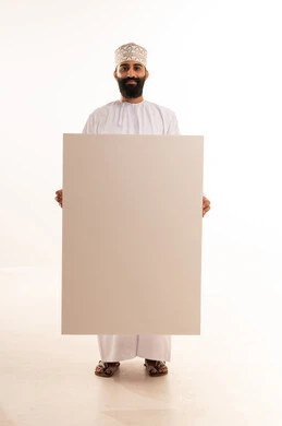Gestures of happiness and joy, advertisements and marketing offers, use of illustrative boards and educational tools, a portrait of a smiling Arab Gulf Omani man wearing a dishdasha and a kumma holding a large white board (empty mock-up) in his hand, full body length, white background.