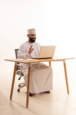 Focusing on task completion, integrating modern technologies in the administrative and office field, working in Omani offices and companies, a portrait of an Arab Gulf Omani man wearing a dishdasha and kumma sitting on an office chair and working on a laptop, white background.