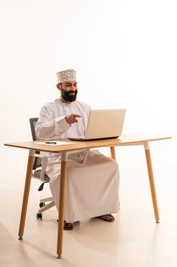 Focusing on task completion, integrating modern technologies in the administrative and office field, working in Omani offices and companies, a portrait of an Arab Gulf Omani man wearing a dishdasha and kumma sitting on an office chair and working on a laptop, white background.