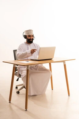 Integrating modern technologies into the administrative and office field, focusing on task completion, listening to music through headphones, working in Omani offices and companies, a portrait of an Arab Gulf Omani man wearing a dishdasha and kumma with headphones sitting on an office chair working on a laptop, white background.