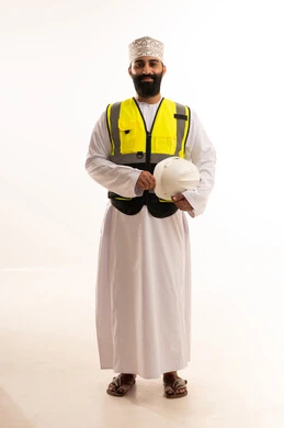 مهنة ووظيفة للشباب في سلطنة عمان، العمل في القطاع الهندسي، مفهوم الهندسة والانشاءات المعمارية، بورتريه لمهندس عربي خليجي عماني يرتدي الدشداشة والكمة وسترة الحماية يمسك بيده الخوذة البيضاء بتعابير السرور،الجسم بالطول الكامل، خلفية بيضاء
