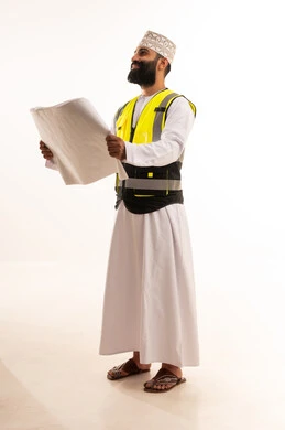 الإشراف على مخططات المشاريع الهندسية،  مفهوم الانشاءات المعمارية، بورتريه لمهندس عربي خليجي عماني يرتدي الدشداشة والكمة وسترة الحماية يمسك بيديه المخطط، العمل في مجال الهندسة، مهنة ووظيفة للشباب في سلطنة عمان، الجسم بالطول الكامل، خلفية بيضاء