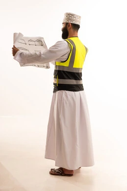 مهنة ووظيفة للشباب في سلطنة عمان، مفهوم الانشاءات المعمارية، بورتريه لمهندس عربي خليجي عماني يرتدي الدشداشة والكمة وسترة الحماية يمسك بيديه المخطط، العمل في مجال الهندسة،الإشراف على مخططات المشاريع الهندسية، الجسم بالطول الكامل، خلفية بيضاء