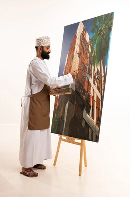 بورتريه لرسام عربي خليجي عماني يرتدي الدشداشة والكمة وقبعة يحمل بيديه الالوان المائية, استخدام ريشة التلوين، أنشطة ترفيهية فنية ممتعة، ورشة عمل وفنون, خلفية بيضاء