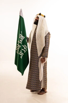 The day we started was 1727 AD, the anniversary of the establishment of the first Saudi state on February 22, the commemoration of Saudi National Day on September 23, a portrait of an Arab Saudi Gulf man wearing a bisht, ghutrah, and agal on the day of establishment raising the Saudi flag, Flag Day on March 11, white background.