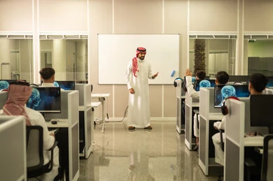 The concept of diligence and striving for excellence: A Saudi Arabian teacher, wearing a traditional thobe and shemagh, discusses lessons with his students. Education in Saudi Arabia: Arab students sit in front of computers in a computer lab.